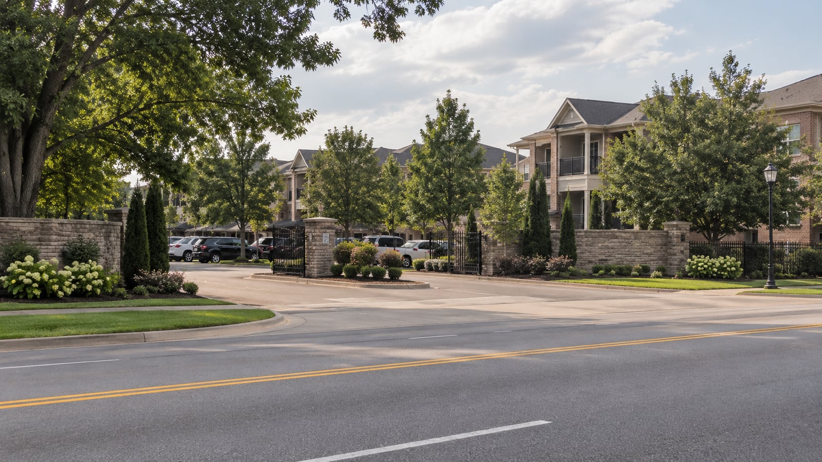Newer apartment community entrance along a suburban road in Collierville Tennessee, gated entry with landscaped monument sign and residential buildings visible behind screening trees