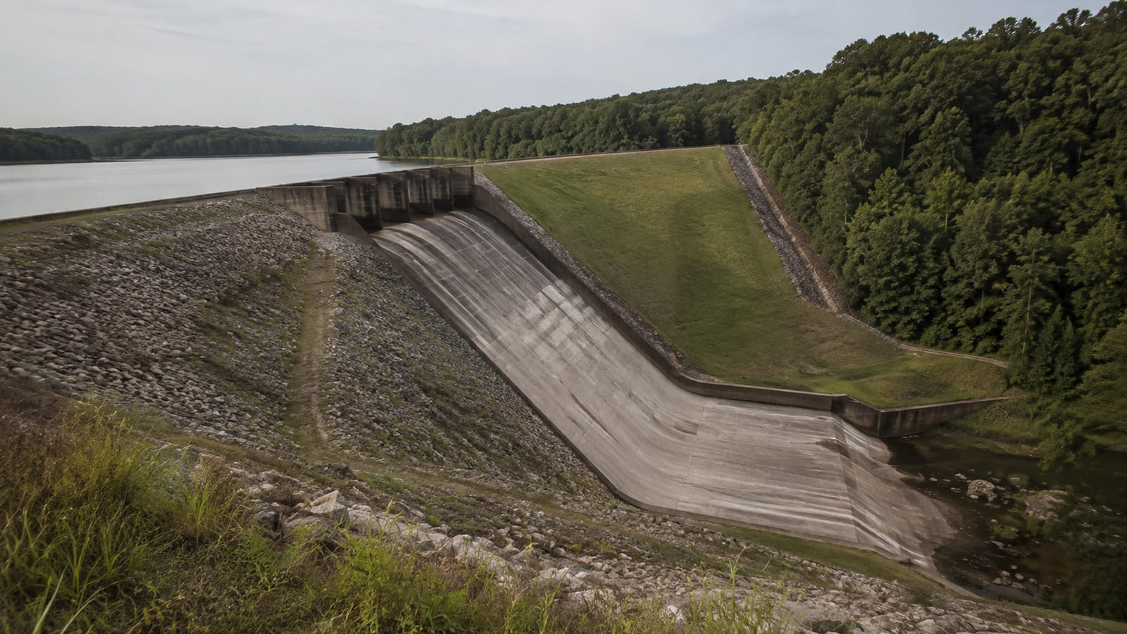 An earthen flood-control dam and concrete spillway at a rural Mississippi reservoir, showing the scale of the infrastructure built to manage the Coldwater River watershed.