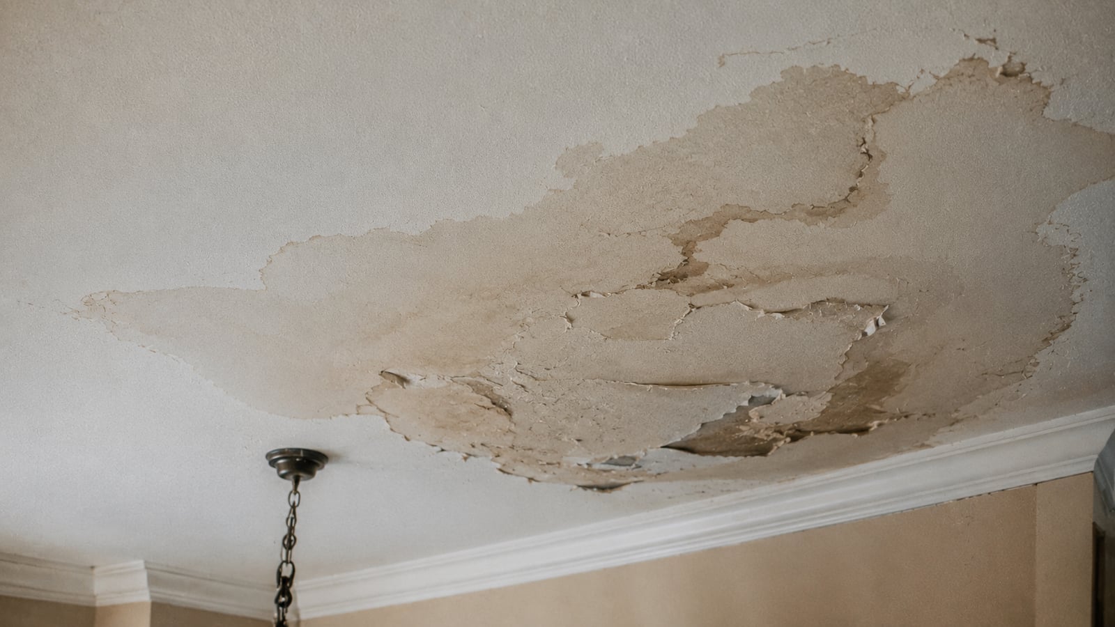 Water stain and peeling paint on an apartment ceiling from an upstairs pipe leak
