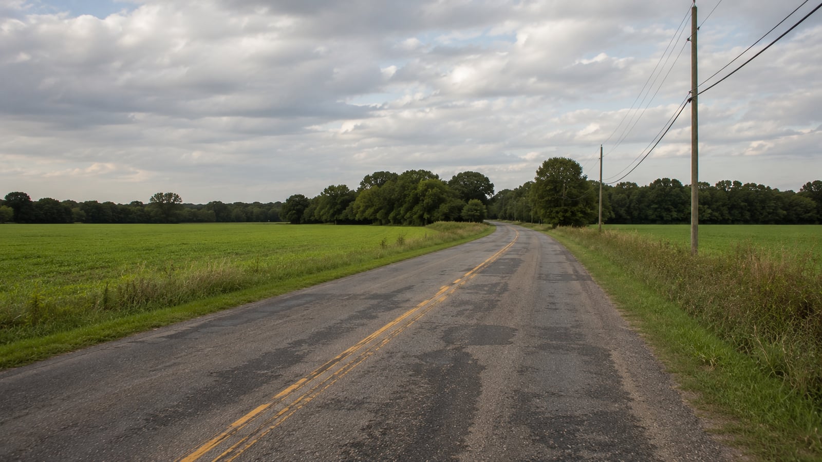 Two-lane DeSoto County Mississippi road with patched asphalt surface curving through flat north Mississippi farmland